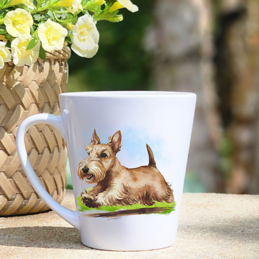 A white ceramic latte mug featuring a Wheaten Scottish Terrier running on a grassy surface.  A basket containing yellow flowers sits to the left-hand side. 