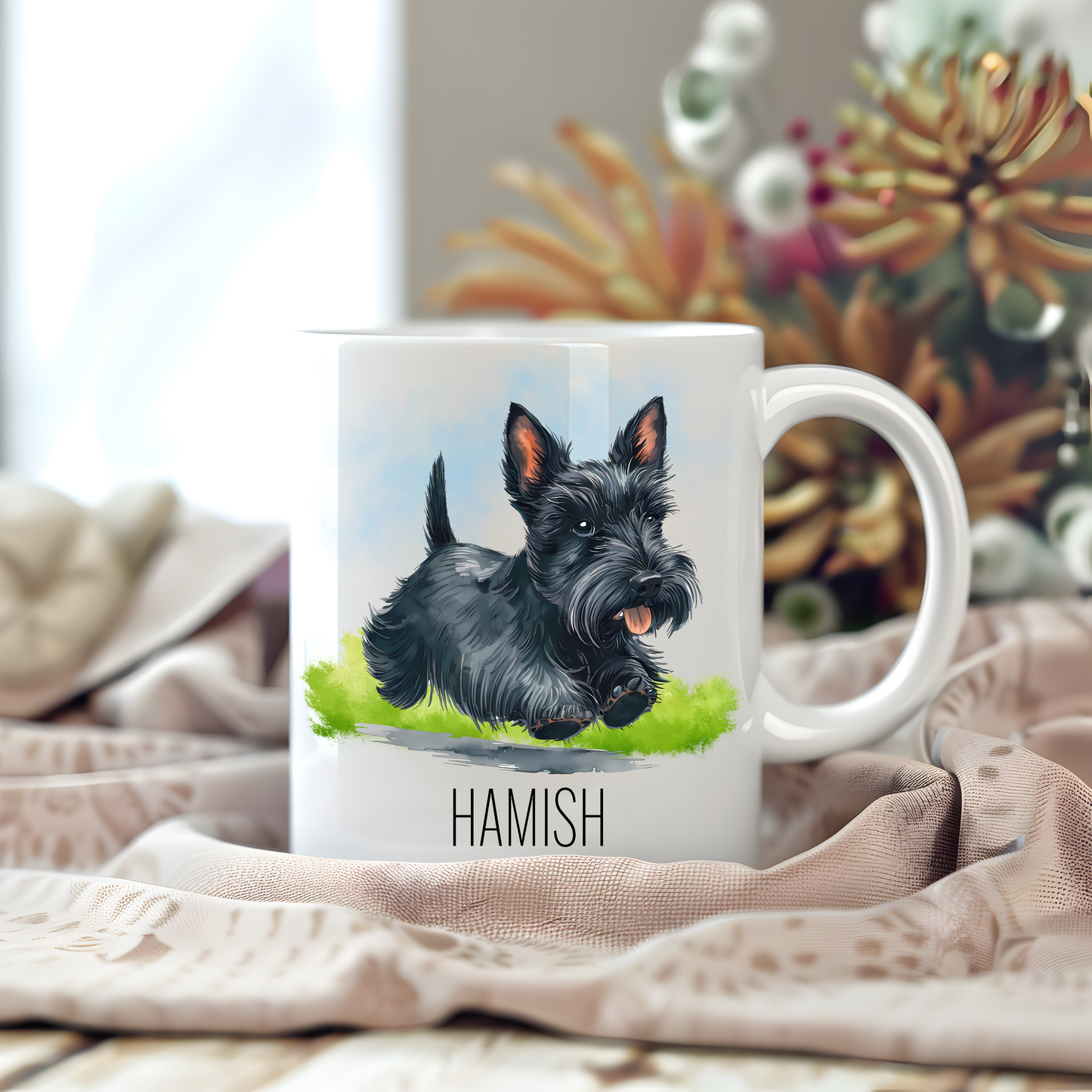 A white ceramic mug with a vibrant image of a black Scottish Terrier sits on a beige tablecloth placed on a wooden surface.  The mug is personalised with a pet name and stems of large flowers decorate the background.