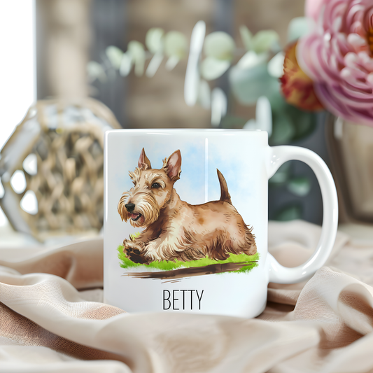 A wjheaten Scottish Terrier running to its right is placed on a white personalised ceramic mug. The mug sits on a beige cloth with a large pink flower and green foliage accessorizing the background.
