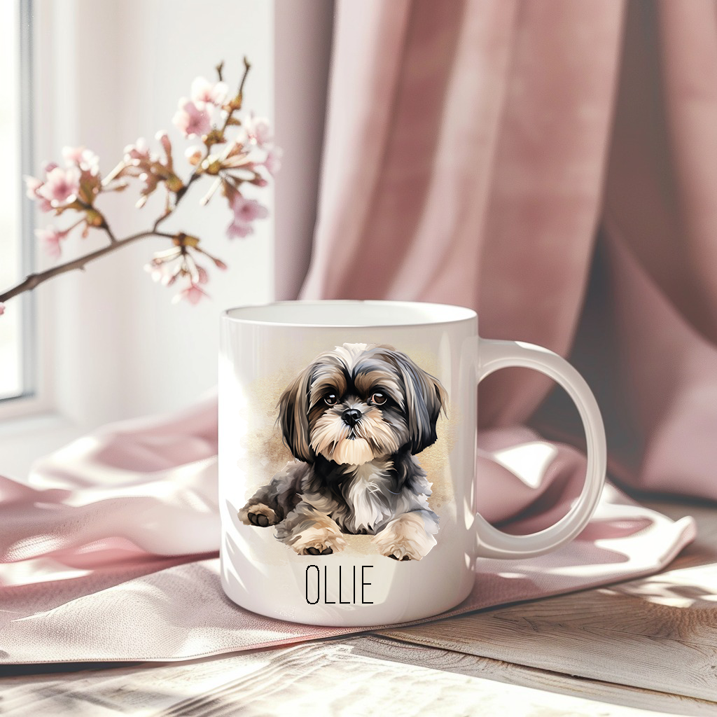 A pink drape creates the backdrop for white ceramic mug with the image of a Shih Tzu dog laid down and looking forward.  A stem of small pink flowers accessorizes the image