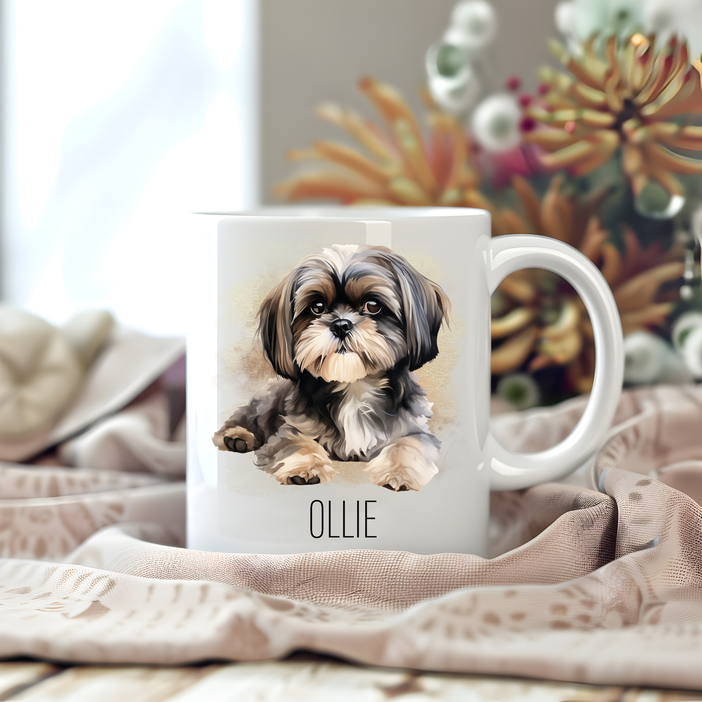 A white ceramic mug with a vibrant image of a Shih Tzu sits on a beige tablecloth placed on a wooden surface.  The mug is personalised with a pet name and stems of large flowers decorate the background.