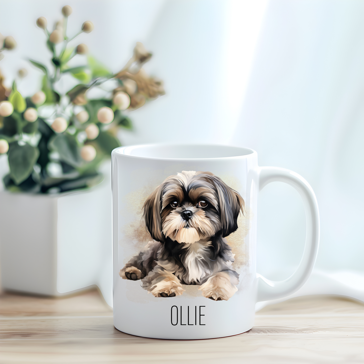 This coffee mug features a Shih Tzu on a white ceramic mug which has been placed on a light wooden surface.  A green and white plant sits on the left side of the image in a square plant pot.

