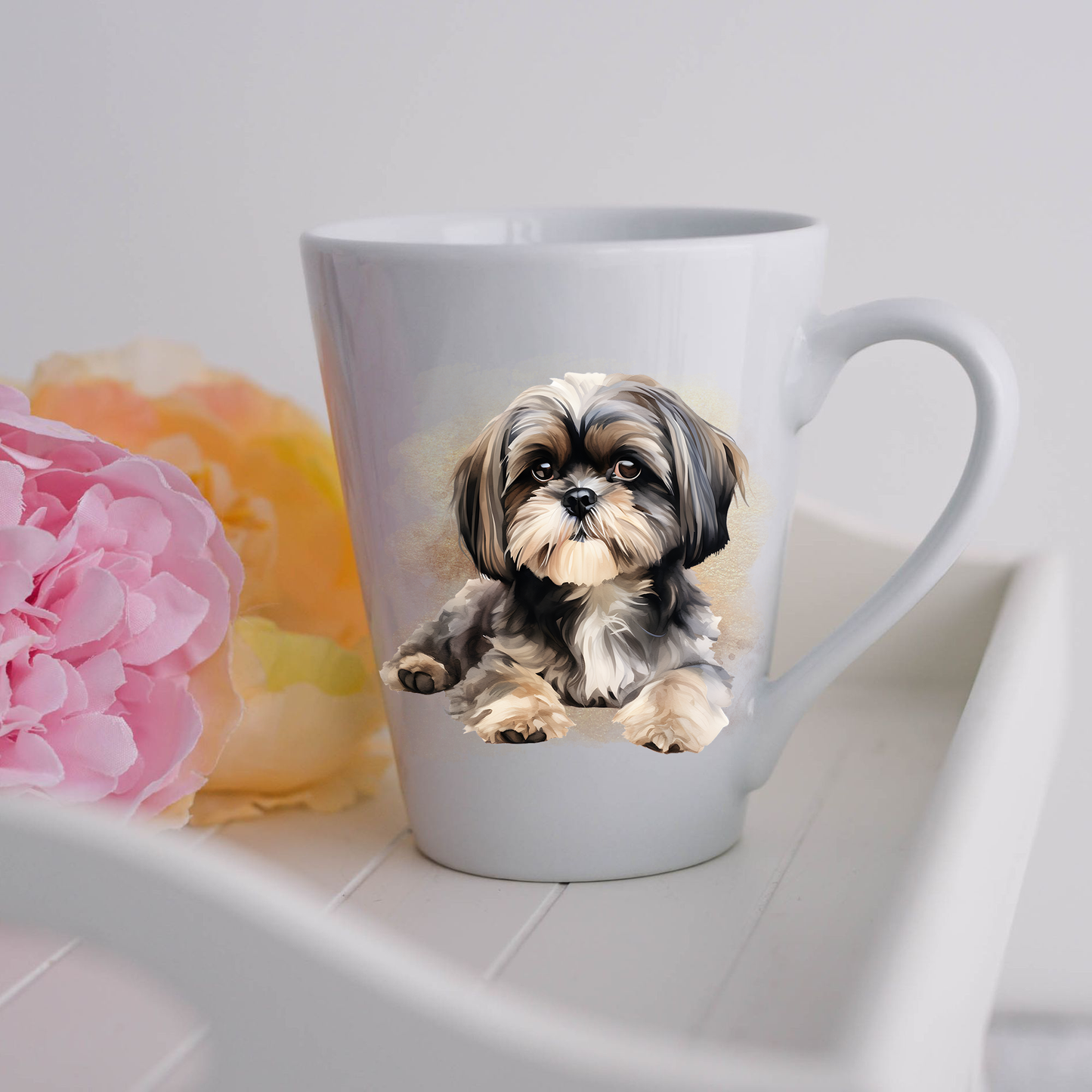 A Shih Tzu is seen on a white ceramic latte mug with a smoky background.  The mug is placed on a white tray with pink and yellow flowers. 