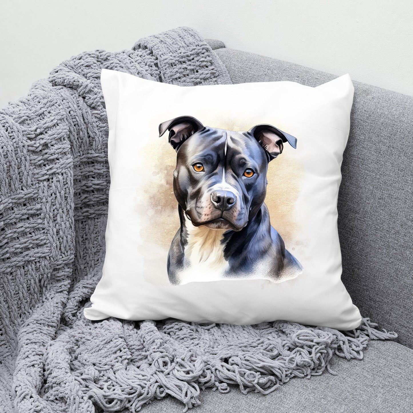 White sofa cushion with an image of a black Staffordshire Bull Terrier with a white chest sat gazing forward.  The cushion is placed on a grey sofa with a grey blanket draped across the corner
