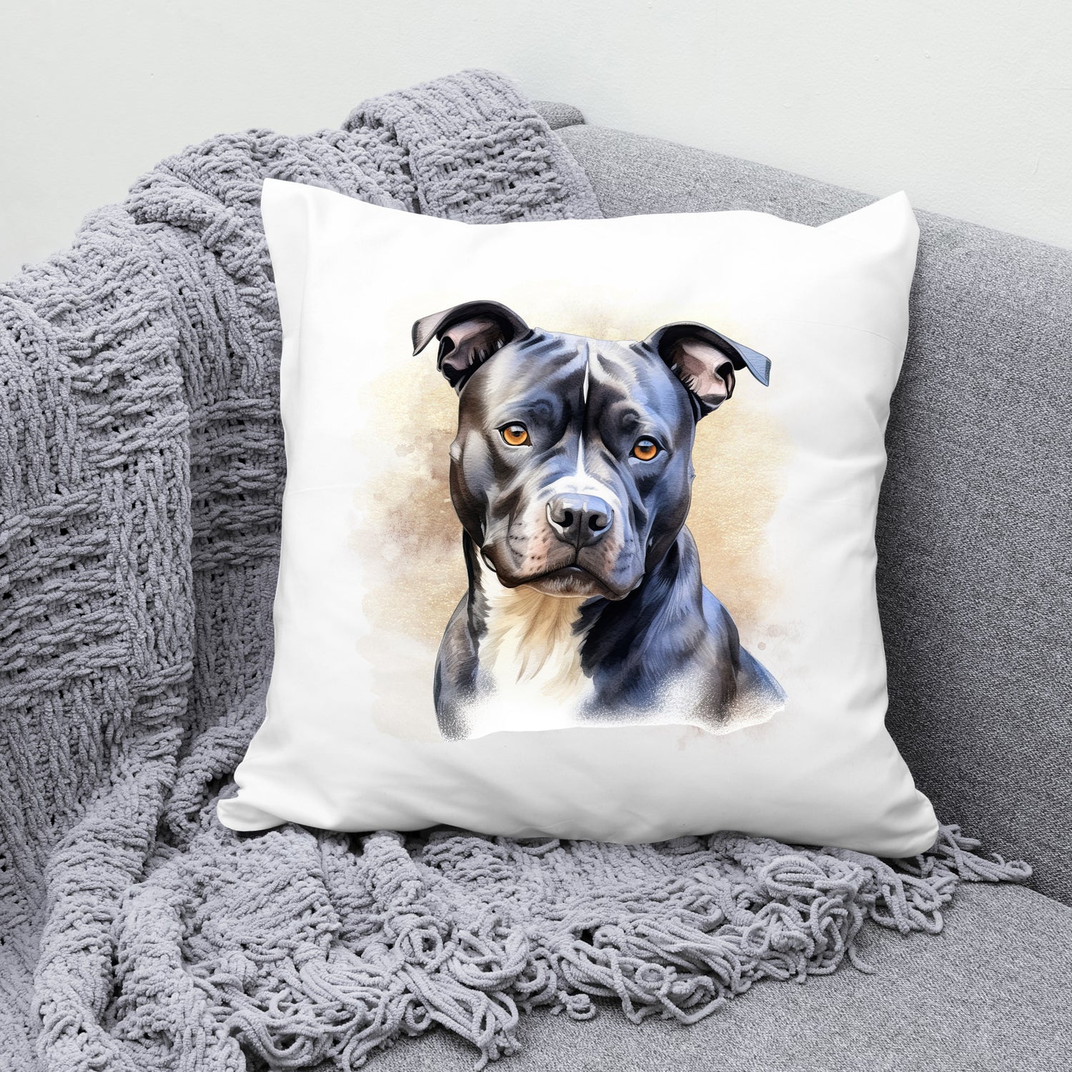 White sofa cushion with an image of a black Staffordshire Bull Terrier with a white chest sat gazing forward.  The cushion is placed on a grey sofa with a grey blanket draped across the corner