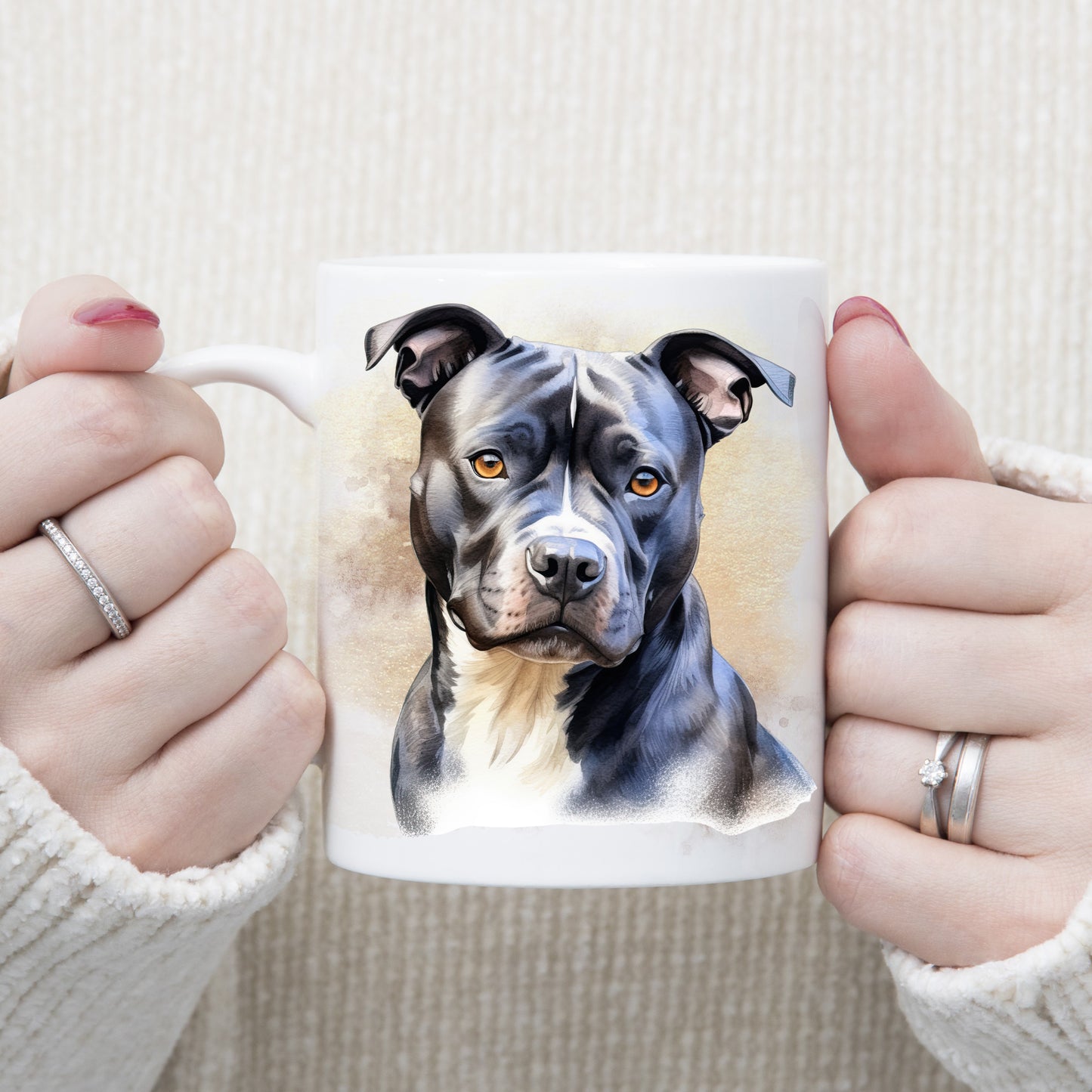 White ceramic mug with an image of a black Staffordshire Bull Terrier with a white chest sat gazing forward. A woman is holding the mug with both hands.