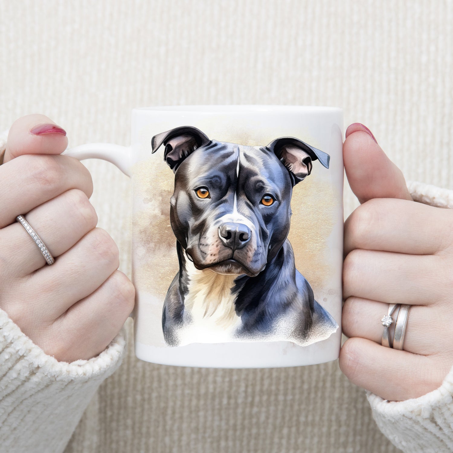 White ceramic mug with an image of a black Staffordshire Bull Terrier with a white chest sat gazing forward. A woman is holding the mug with both hands.