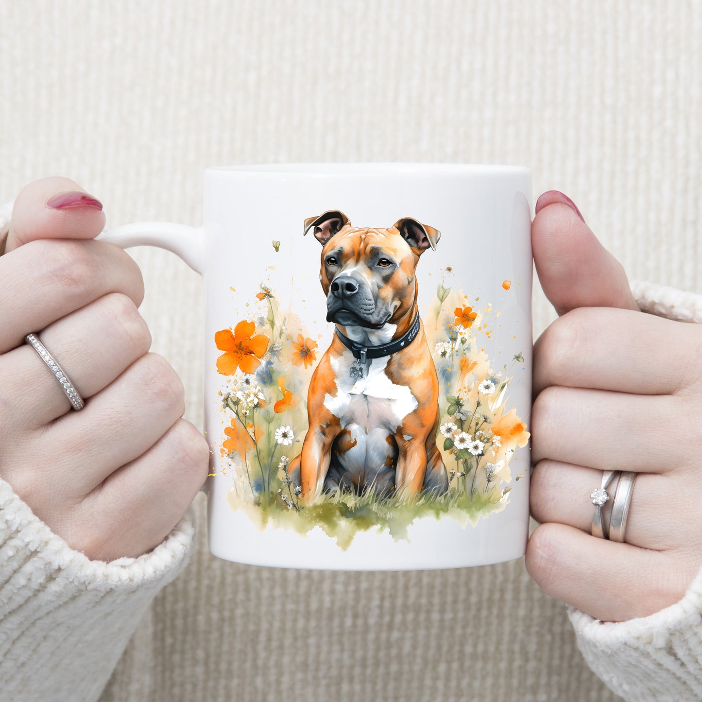 White ceramic mug with an image of a tan Staffordshire Bull Terrier with a white chest sat gazing left.  A woman is holding the mug with both hands.