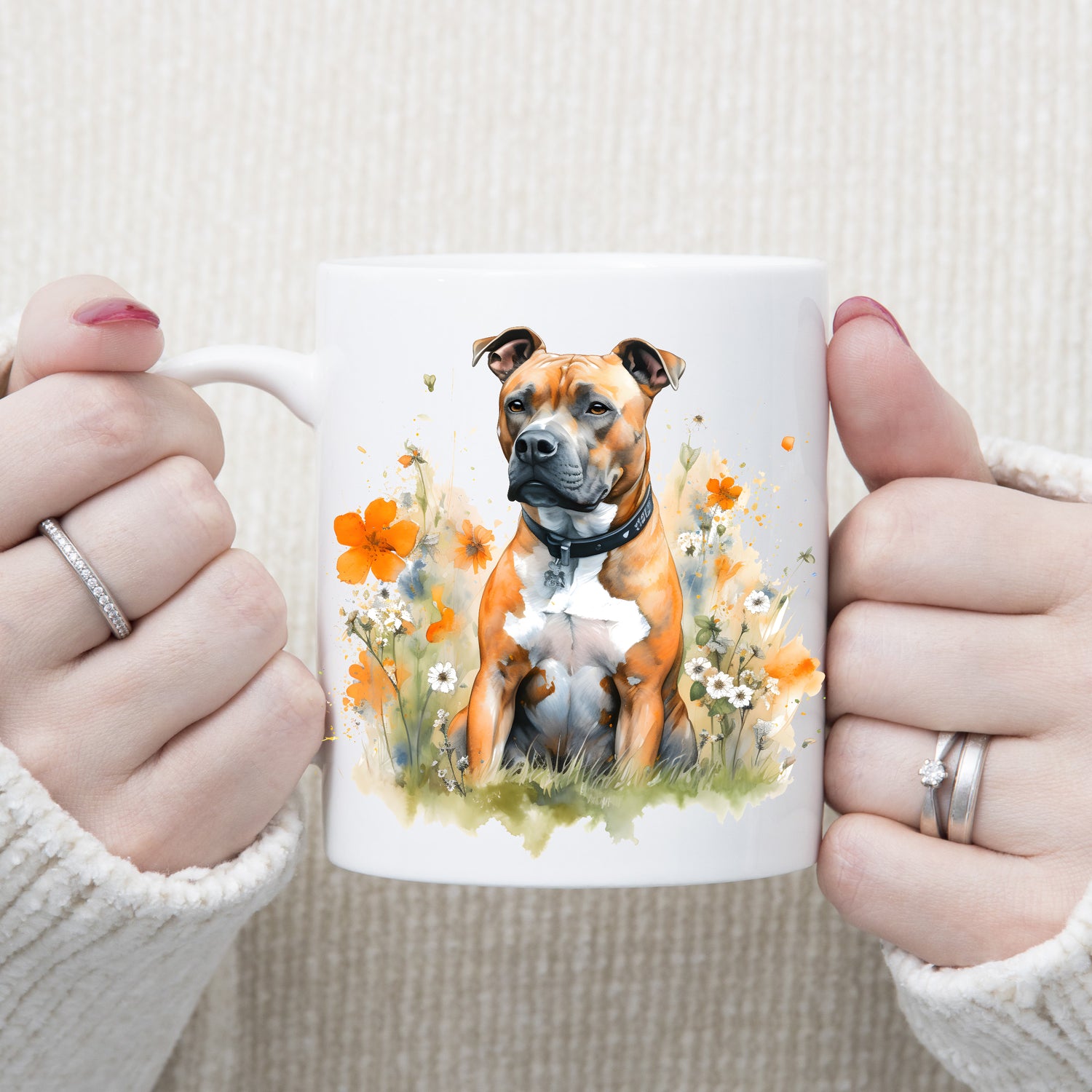 White ceramic mug with an image of a tan Staffordshire Bull Terrier with a white chest sat gazing left.  A woman is holding the mug with both hands.