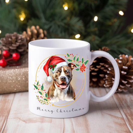 Staffordshire Bull Terrier wearing aChristmas hat on a Christmas themed mug.  Placed on a wooden surface with pine cones and gifts behind.