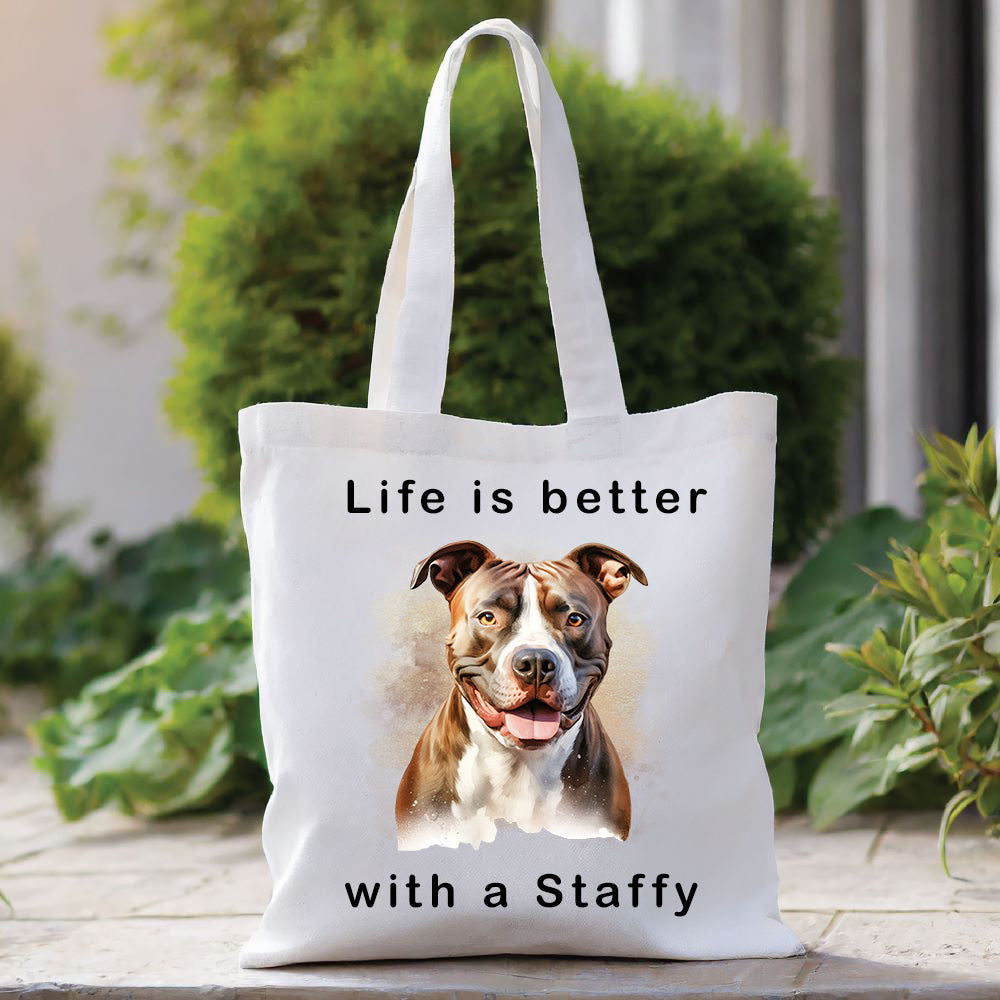 White Tote Bag with a head shot of a brindle Staffordshire Bull Terrier with a white chest sat gazing forward. A quote decorates the bag top and bottom. A green bush sits behind with foliage to the right