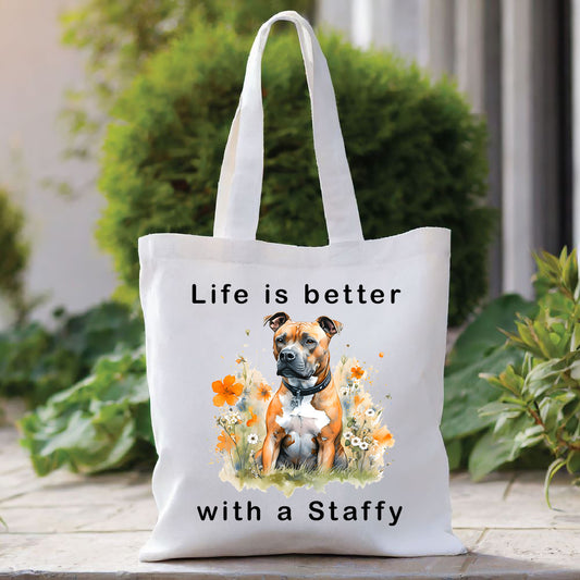 White Tote Bag with an image of a tan Staffordshire Bull Terrier sat among orange flowers and gazing left. A quote decorates the bag top and bottom. A green bush sits behind with foliage to the right
