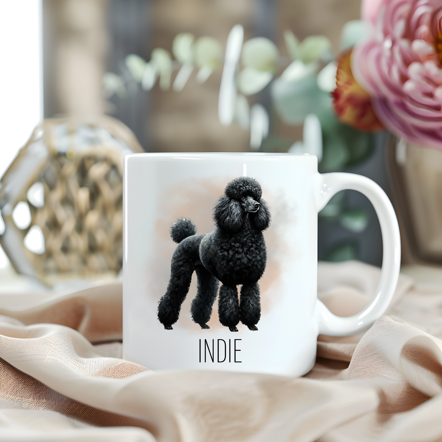 A Standard Poodle stands facing right on a white personalised ceramic mug which has been placed on a beige cloth.  A large pink flower with green foliage accessorizes the image.
