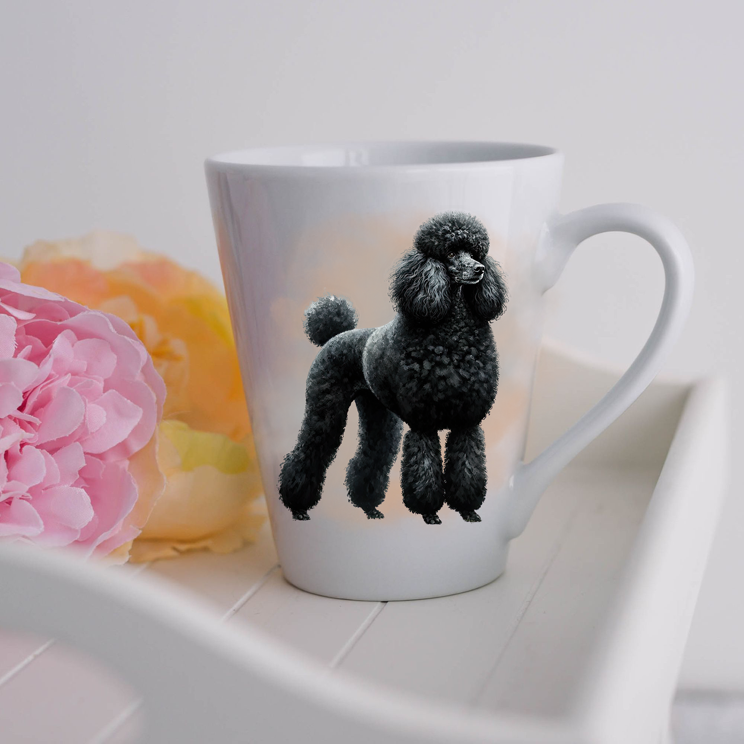 A black Standard Poodle is standing and is placed on a white ceramic latte mug in a smoky background and looking forward.  The mug is placed on a white tray with pink and yellow flowers.