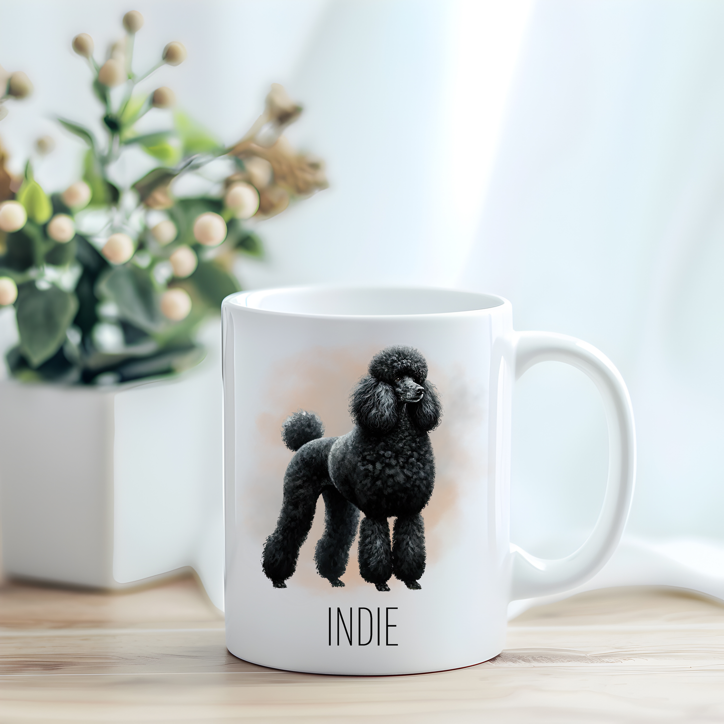 This coffee mug features a Standard Poodle on a white ceramic mug which has been placed on a light wooden surface.  A green and white plant sits on the left side of the image in a square plant pot.