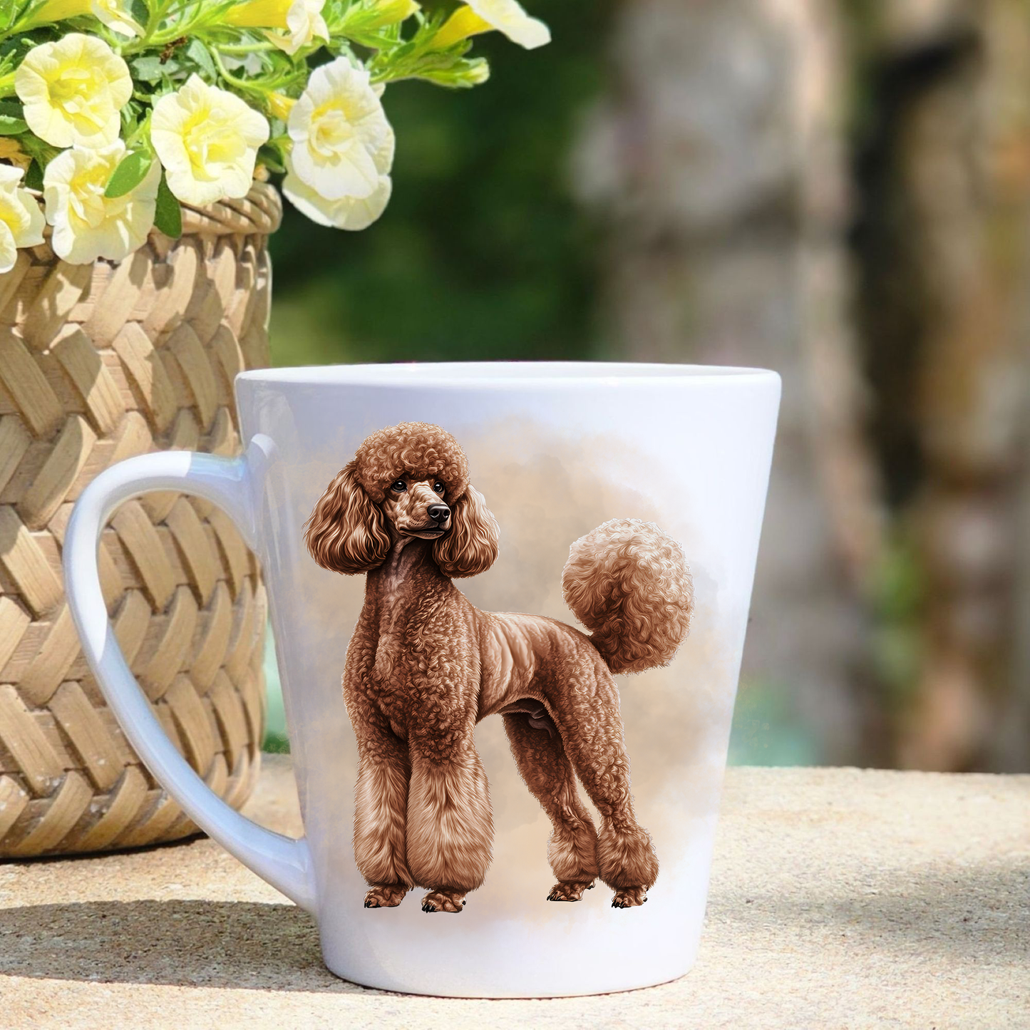 A white ceramic latte mug featuring a brown Standard Poodle is stood  in a beige mist background.  A basket containing yellow flowers sits to the left-hand side.