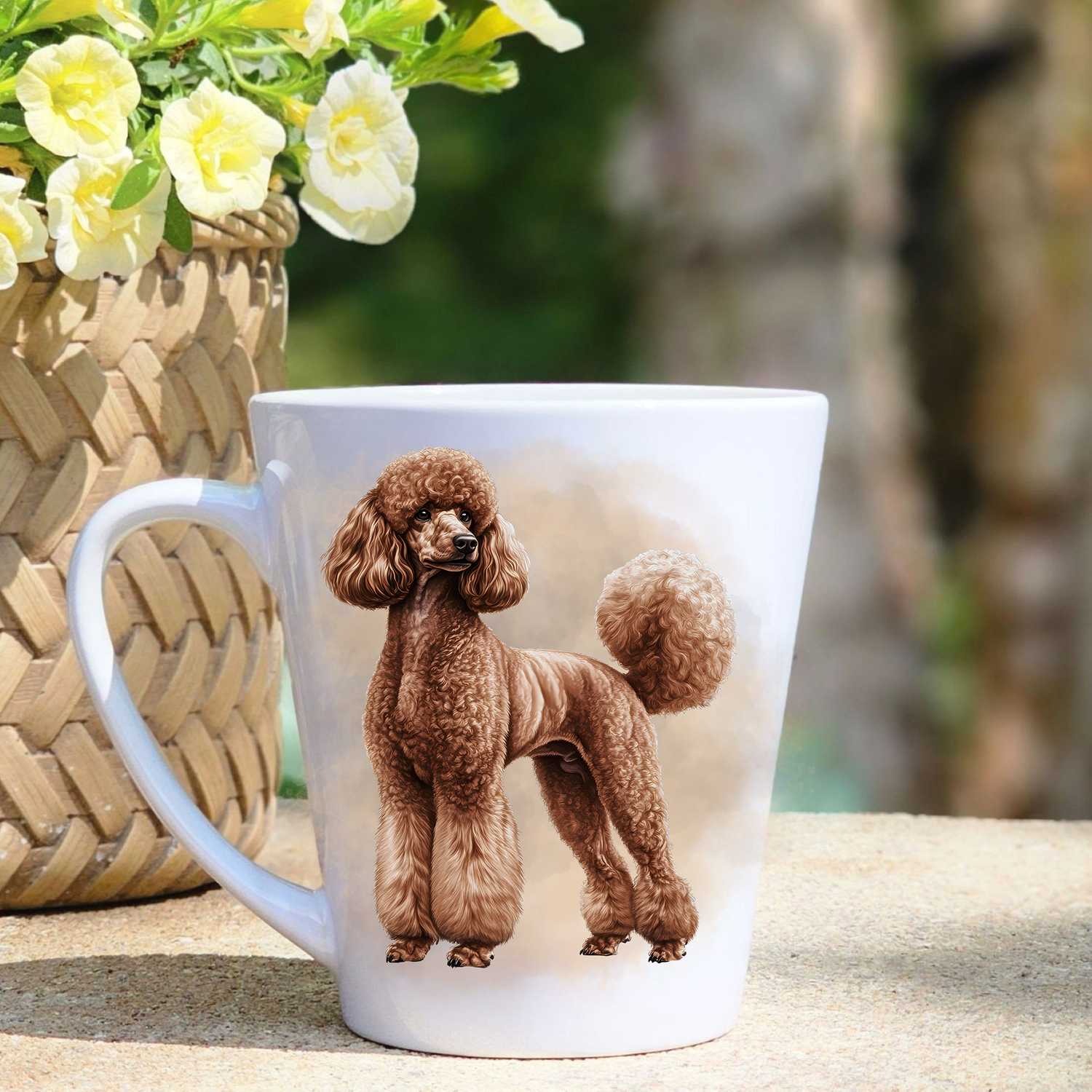 A white ceramic latte mug featuring a brown Standard Poodle is stood  in a beige mist background.  A basket containing yellow flowers sits to the left-hand side.
