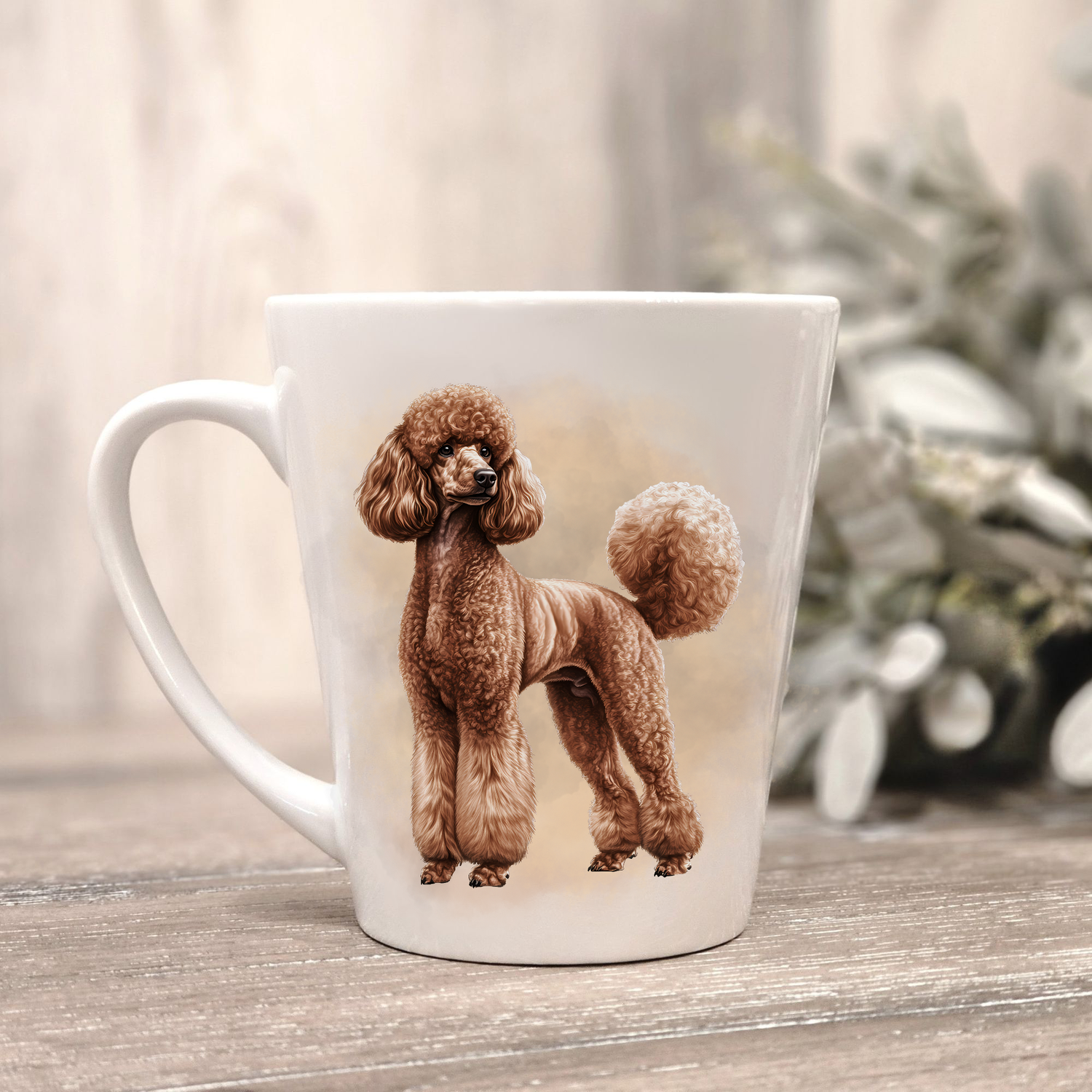 A brown Standard Poodle is shown on a white ceramic latte mug in a smoky background and looking to its left.  The mug is placed on a wooden surface with sage green foliage to the right-hand side.