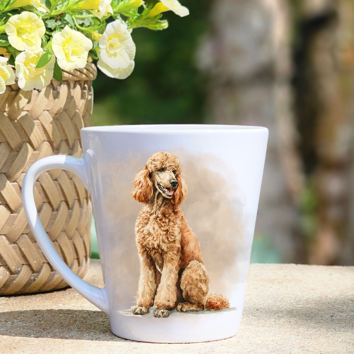 A white ceramic latte mug featuring an Apricot Standard Poodle in a beige mist background.  A basket containing yellow flowers sits to the left-hand side.