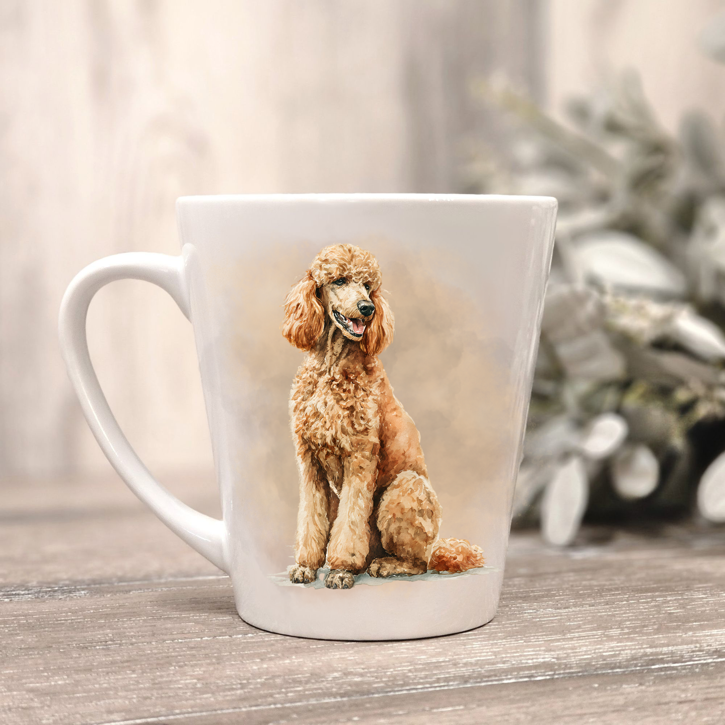 An Apricot Standard Poodle is shown on a white ceramic latte mug in a smoky background and looking to its left.  The mug is placed on a wooden surface with sage green foliage to the right-hand side.