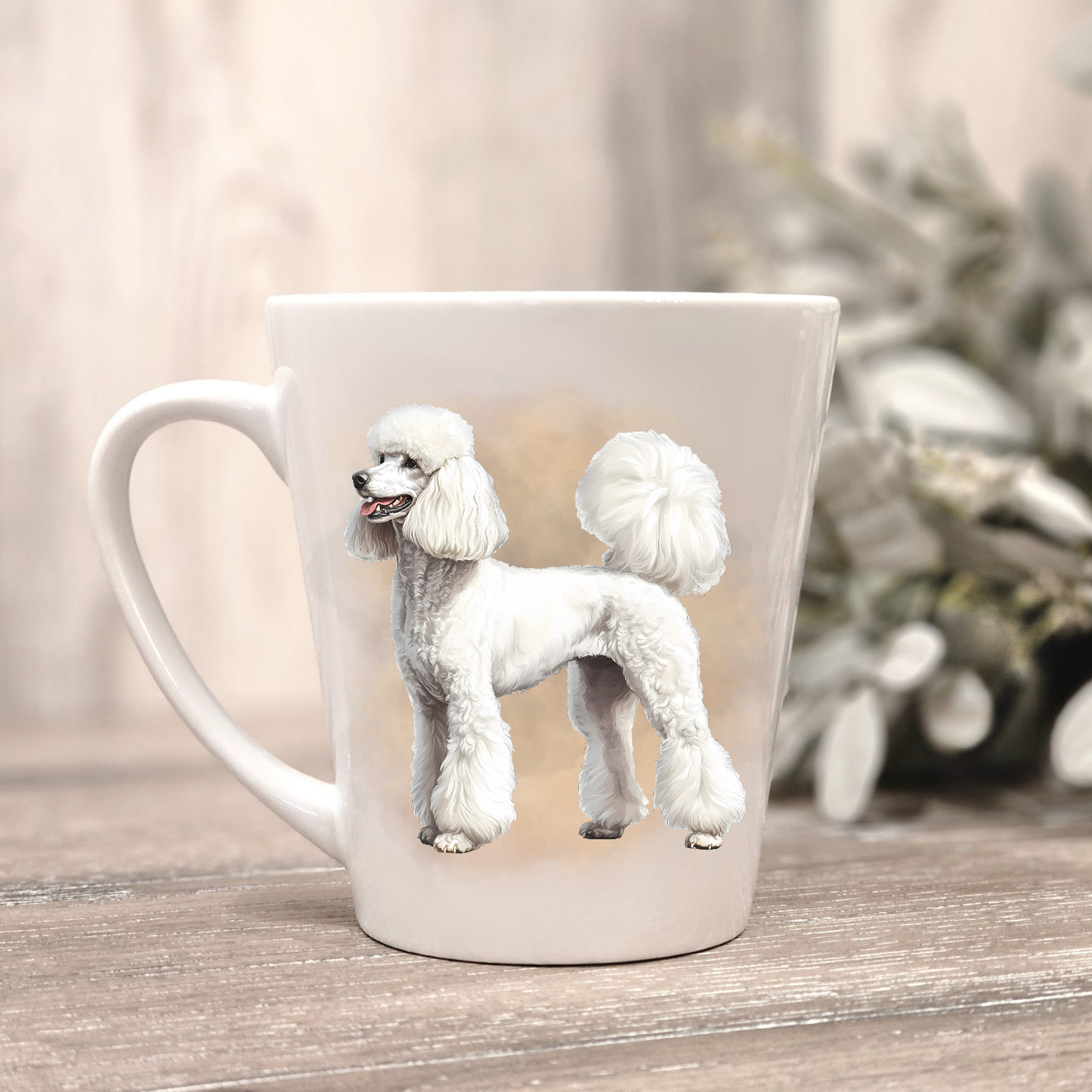 A white Standard Poodle is shown on a white ceramic latte mug in a smoky background and looking to its right.  The mug is placed on a wooden surface with sage green foliage to the right-hand side.
