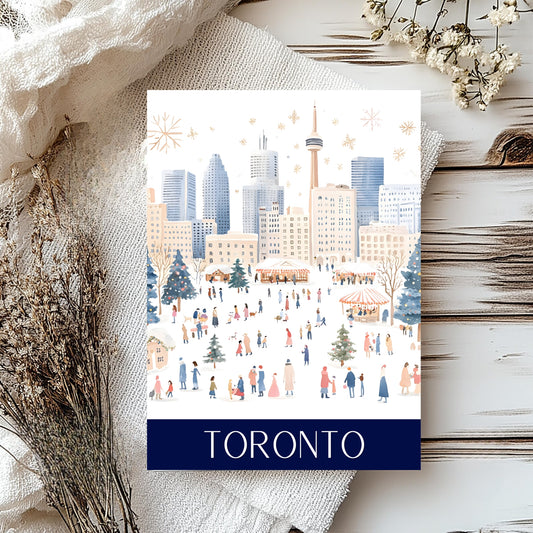 A rectangular travel card featuring a winter city scene labelled TORONTO at the bottom, styled on a white wood surface with a cream fabric and dried floral props.