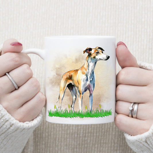 A white ceramic mug shows a tan and white whippet is stood on a grassy surface with yellow flowers. A brown and gold misty background decorates. The mug is being held by a woman.
