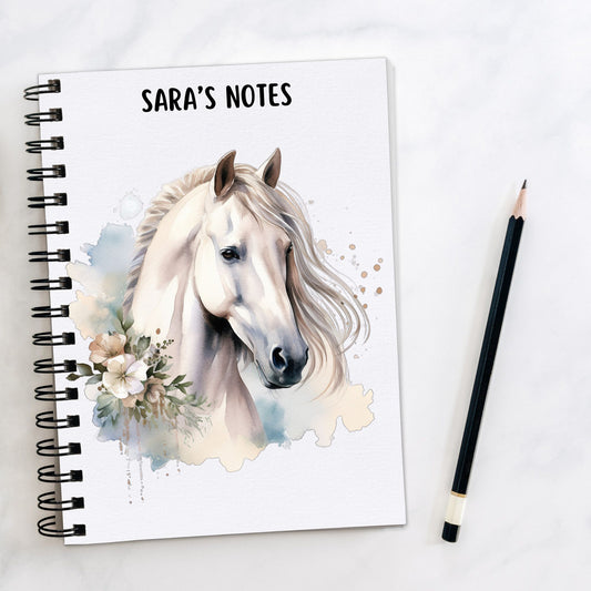 White notebook showing a White horse with a flowing mane. Flowers decorate and a pencil is laid to the side.