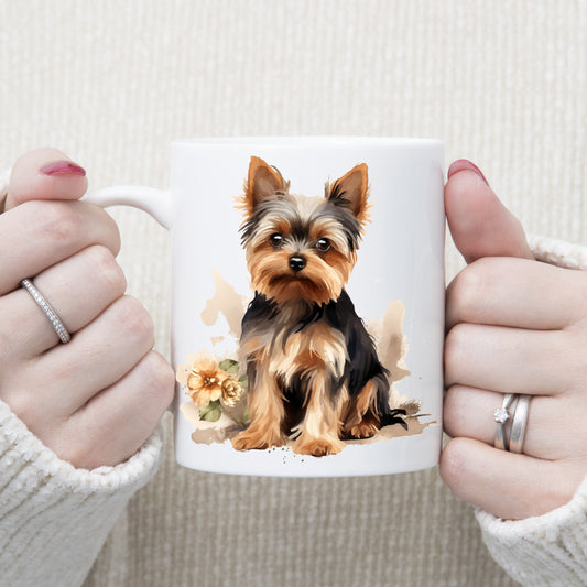 Yorkshire Terrier dog sat on a white ceramic mug.  Yellow flowers decorate.  The mug is being held by a woman with both hands.