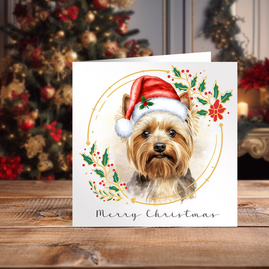 Yorkshire Terrier wearing a Santa hat on a Christmas themed card. Christmas tree in the background.
