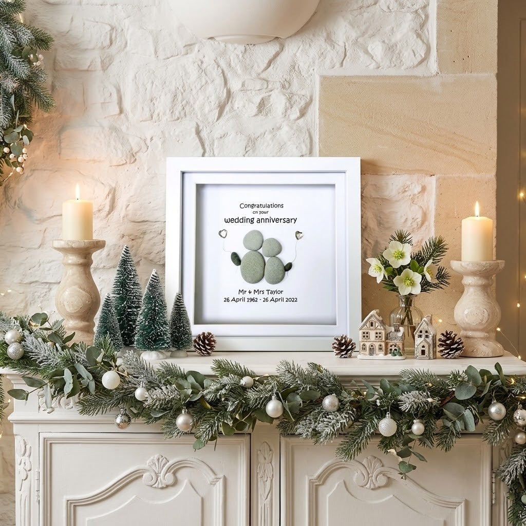 A framed wedding anniversary keepsake with pebble couple displayed on a decorated Christmas mantel.