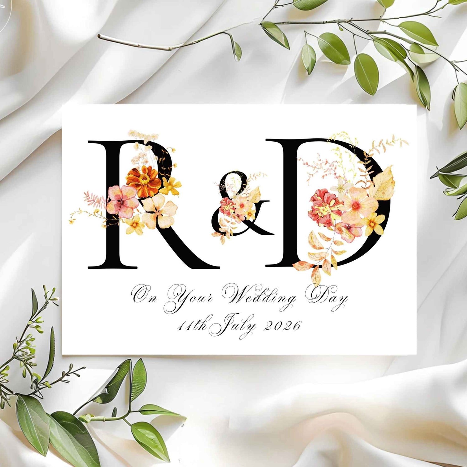 Wedding card with floral initials 'R' & 'D' on a white fabric background.