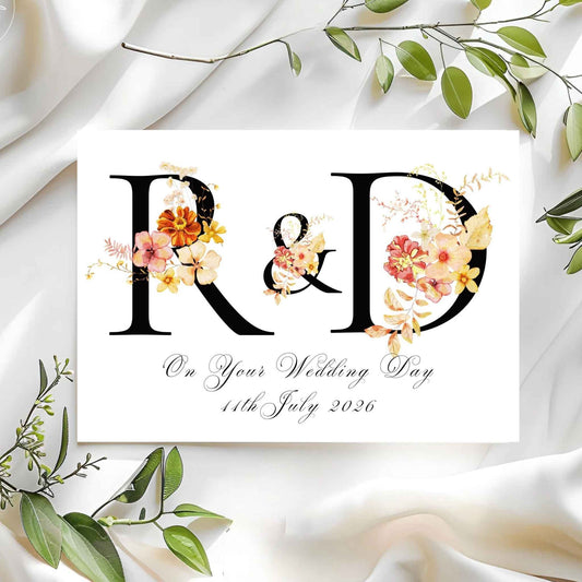 Wedding card with floral initials 'R' & 'D' on a white fabric background.
