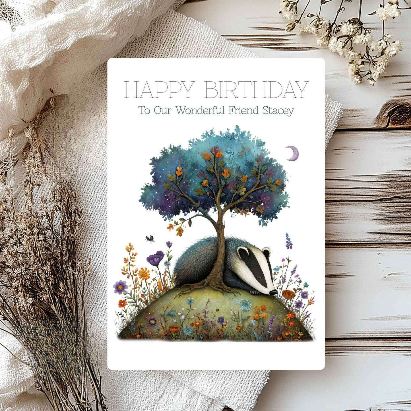 Greeting card with badger and tree illustration on a wooden surface with flowers.