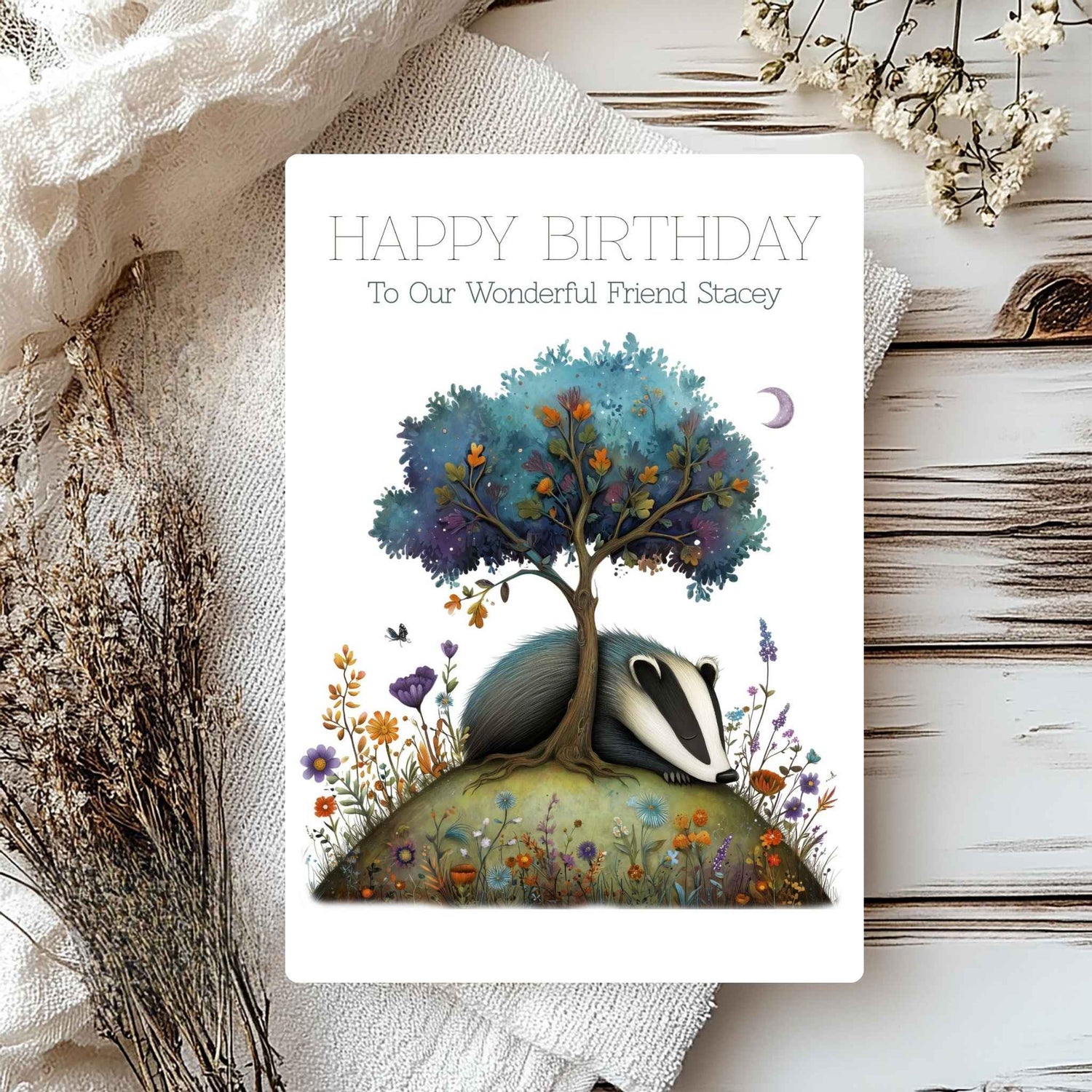 Greeting card with badger and tree illustration on a wooden surface with flowers.