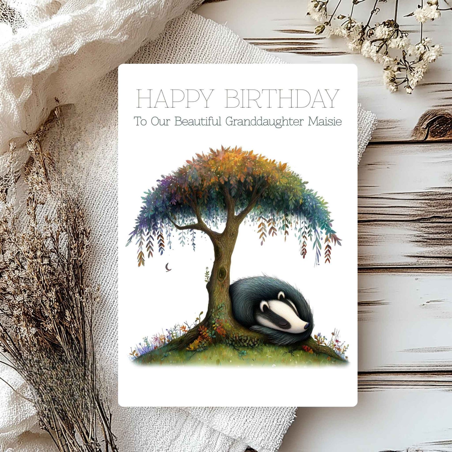 Birthday card with a badger under a tree, surrounded by flowers on a textured surface.
