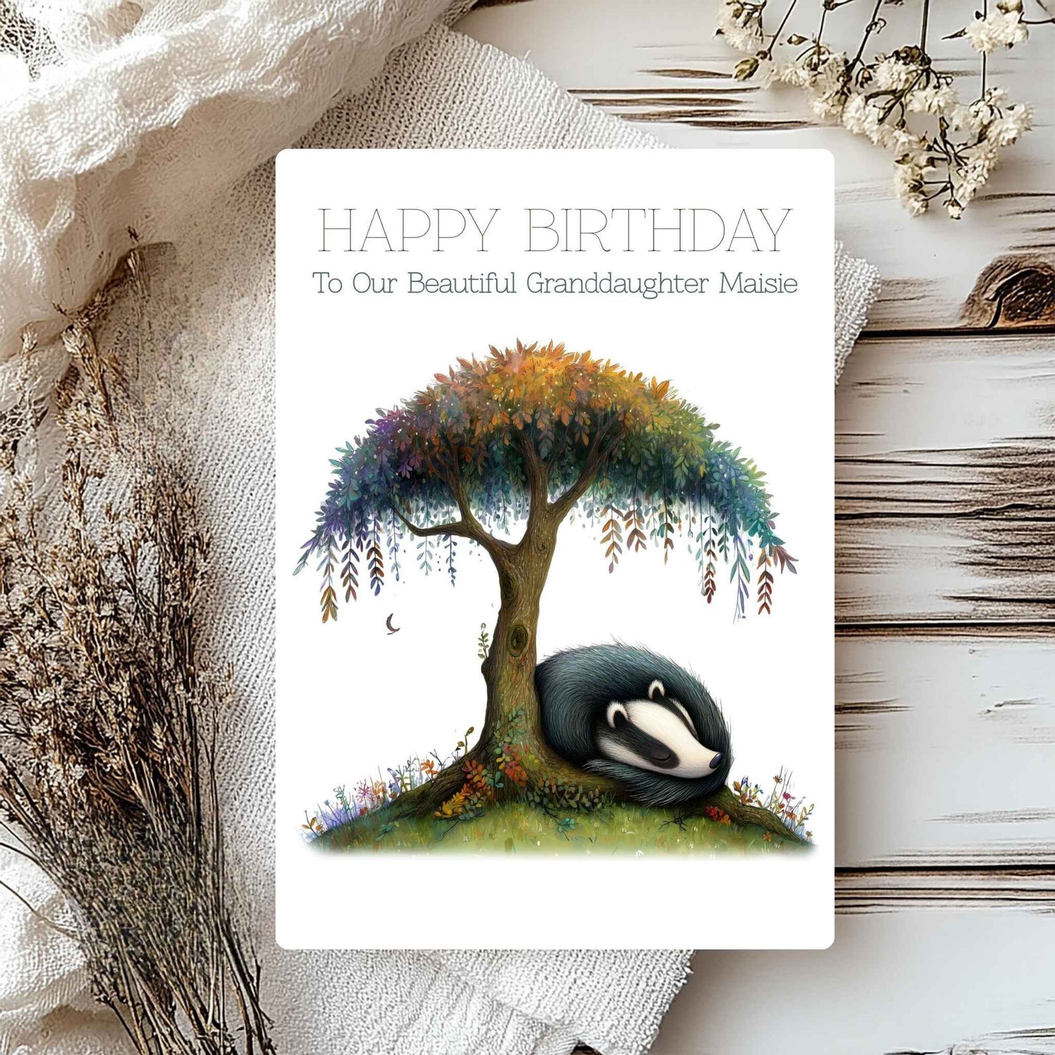 Birthday card with a badger under a tree, surrounded by flowers on a textured surface.