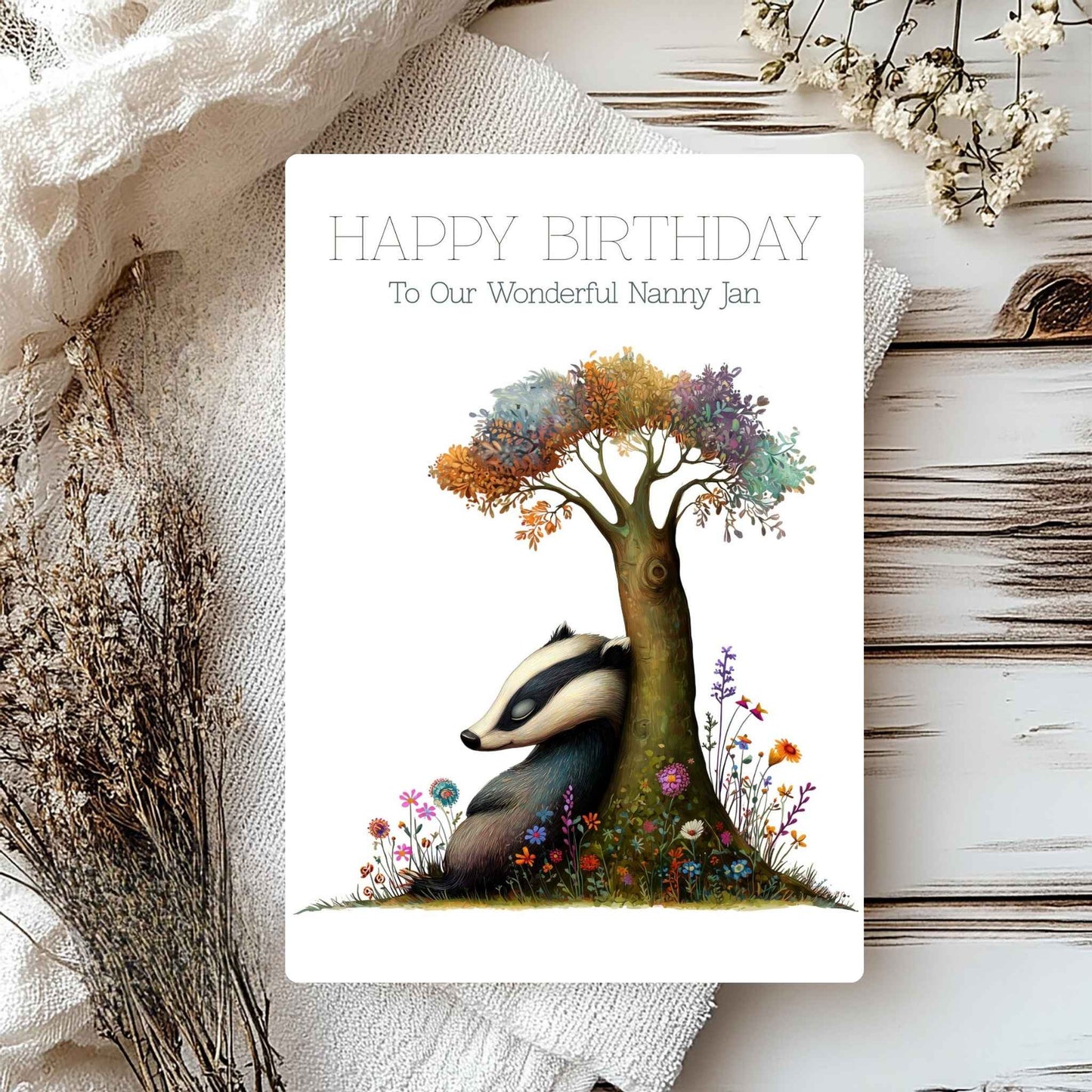 Birthday card with a badger and tree illustration on a textured surface with flowers.