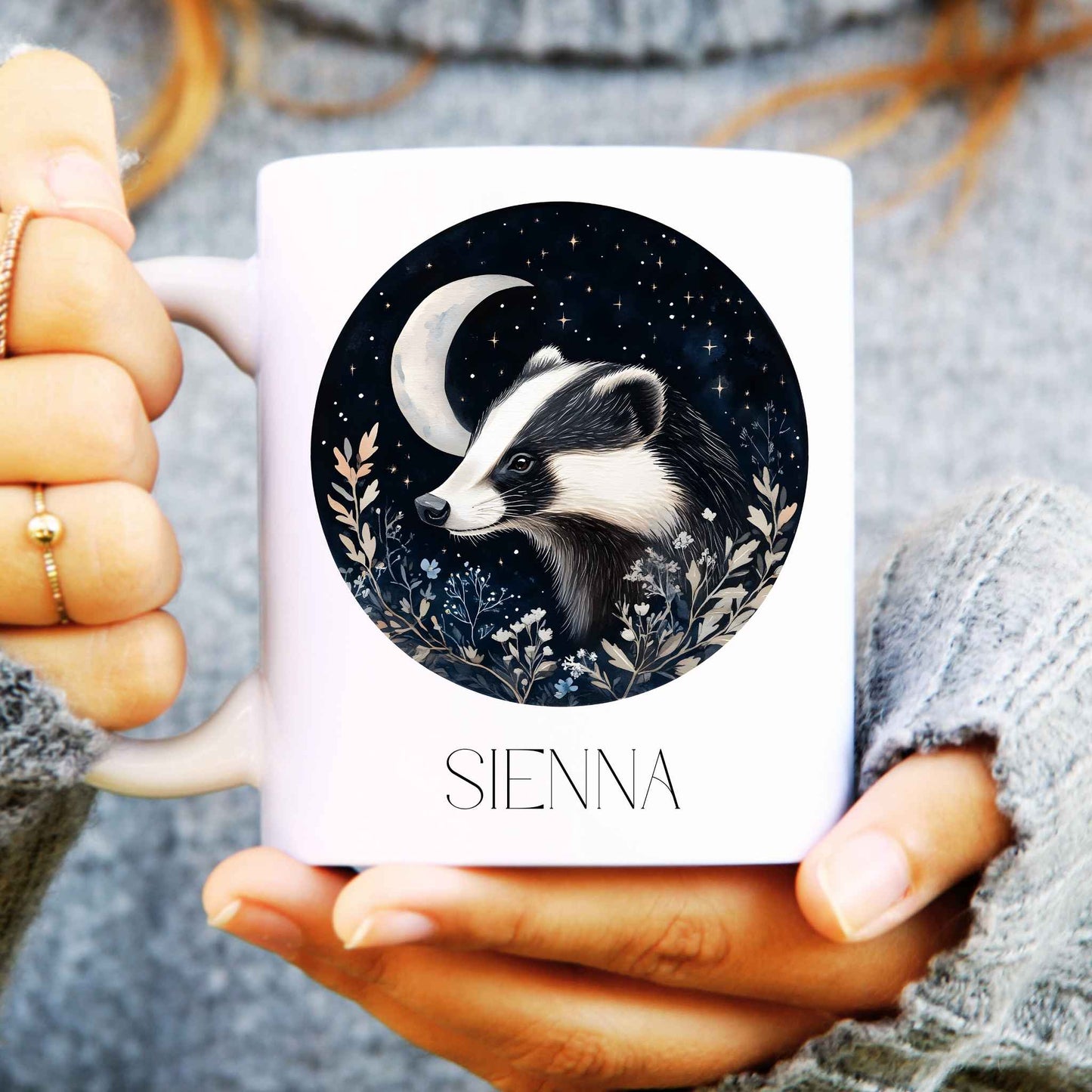 Person holding a mug with a badger design and 'SIENNA' branding.