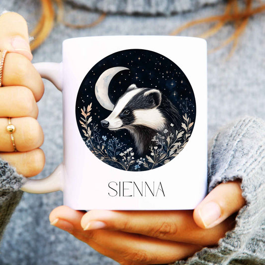 Person holding a mug with a badger design and 'SIENNA' branding.