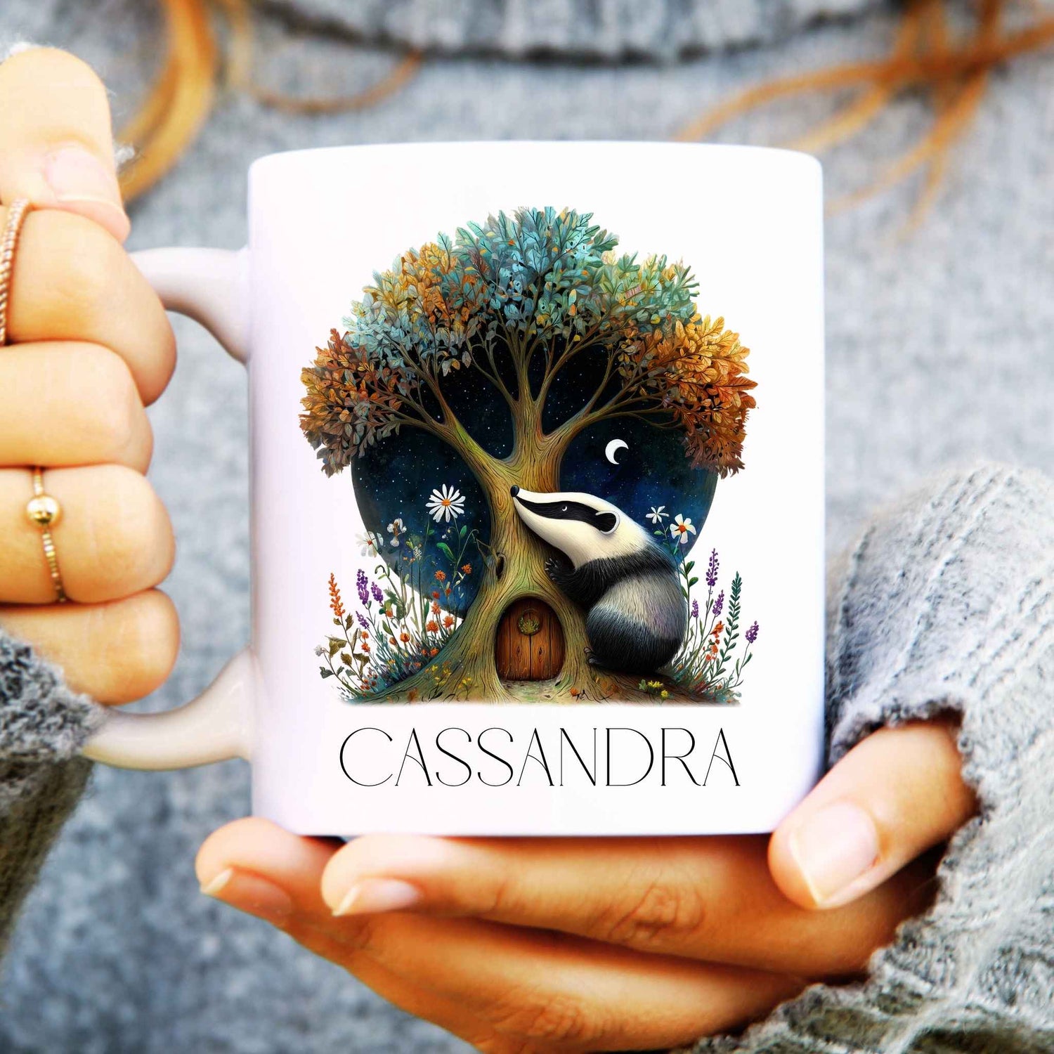 Person holding a mug with a tree and badger design, personalised with 'Cassandra'.