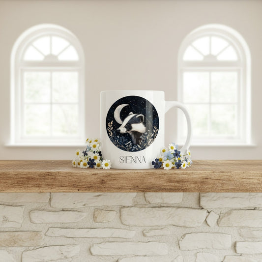 Mug with badger design and 'Sienna' text on a wooden surface with flowers, against a neutral wall.