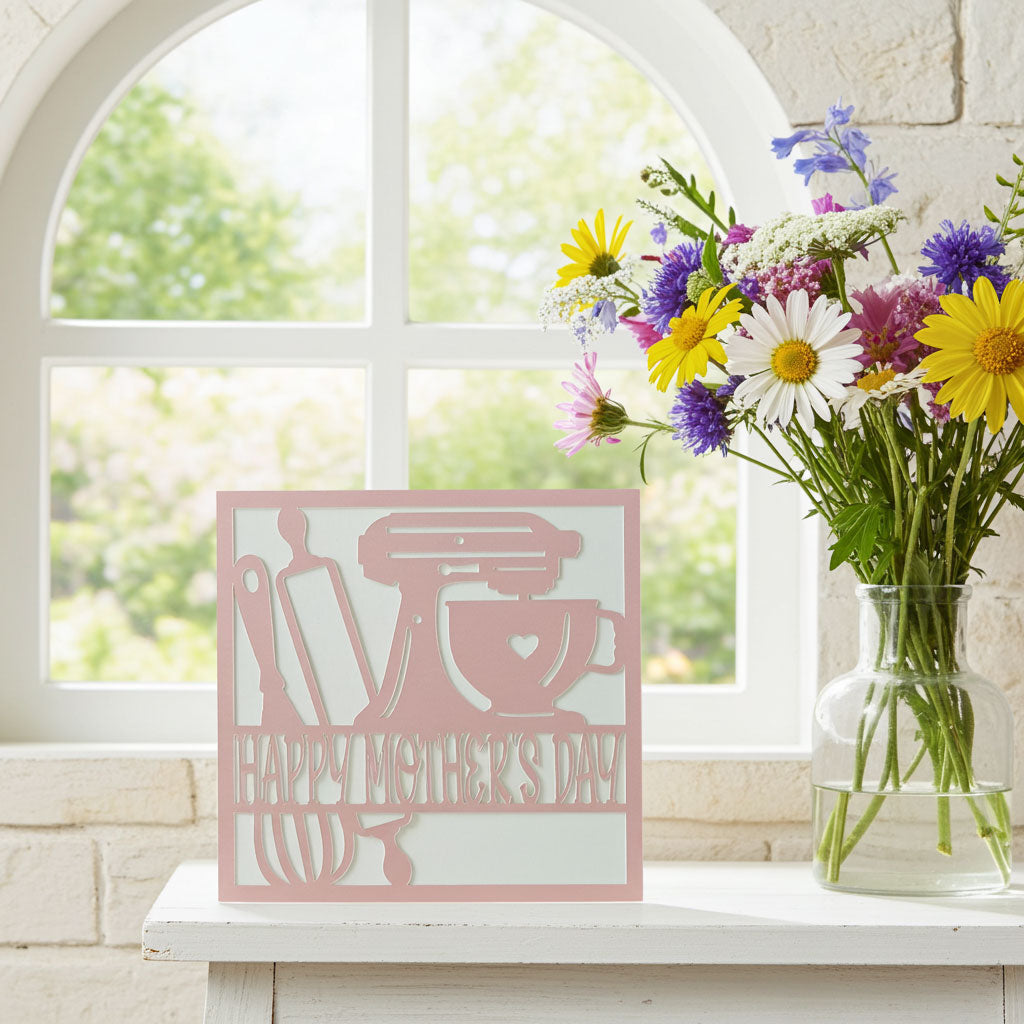 Pink baking Mother's Day card with a vase of flowers on a windowsill.
