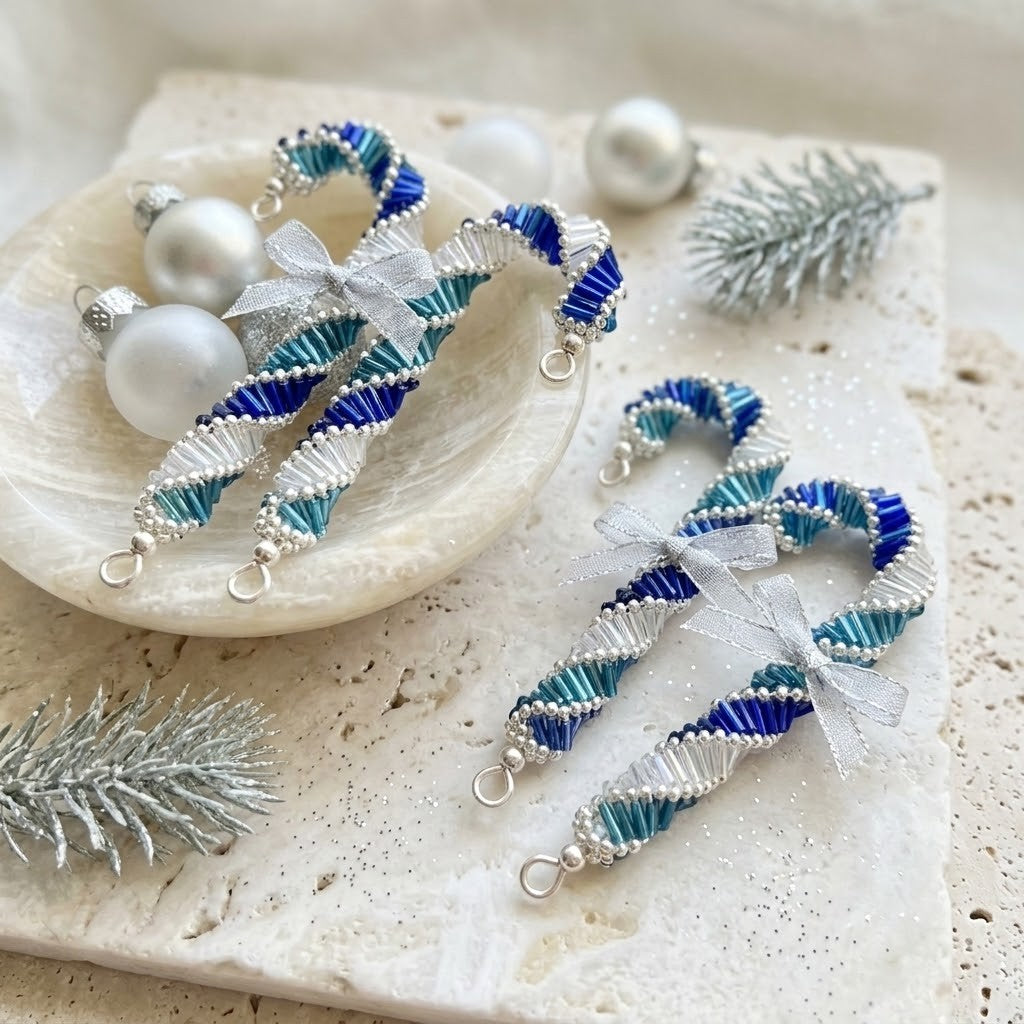 Handmade beaded candy cane ornaments in blue, teal, and white with silver bows and lobster clasps, displayed on a textured stone surface with decorative pearls and silver pine branches.