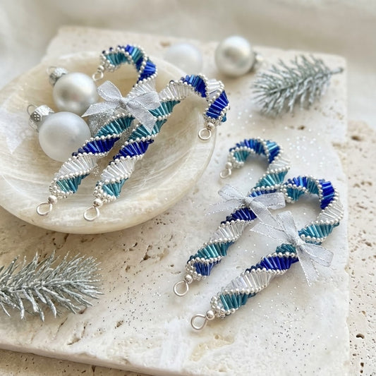 Handmade beaded candy cane ornaments in blue, teal, and white with silver bows and lobster clasps, displayed on a textured stone surface with decorative pearls and silver pine branches.