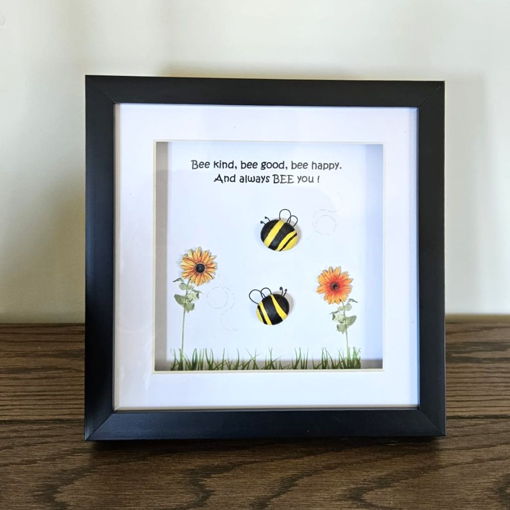 Framed artwork with bees and flowers on a wooden surface