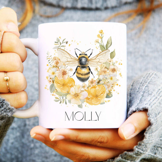 Person holding a mug with a bee and floral design, personalized with 'MOLLY'.