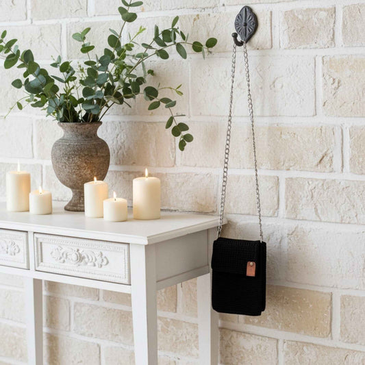 Black phone handbag hanging on a hook above a white console table with candles and a plant.