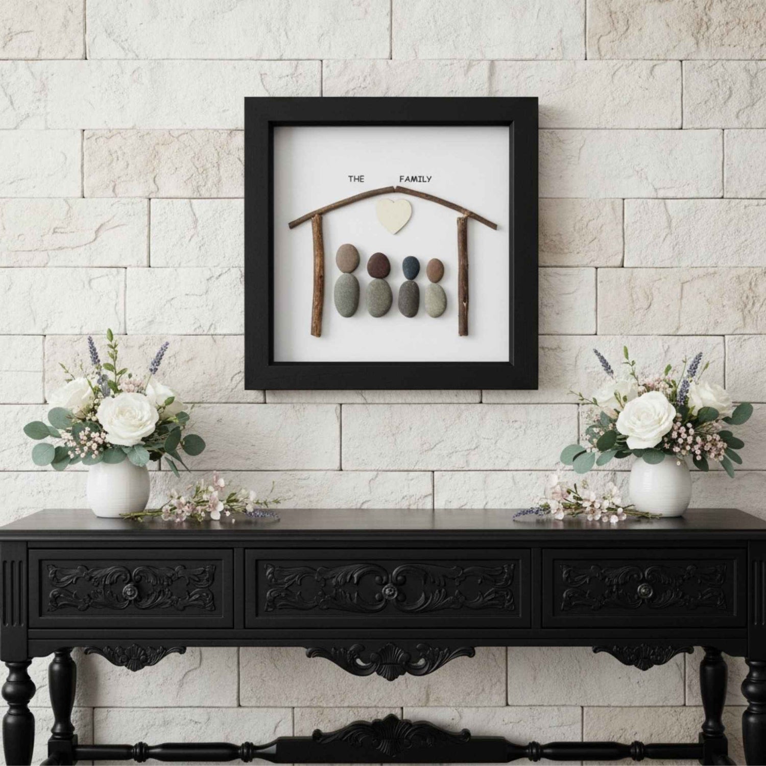 Decorative wall art with pebbles on a black frame above a black console table with floral arrangements.