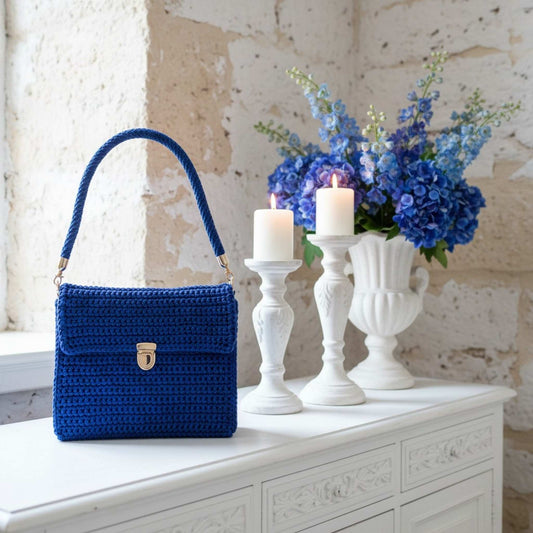 Blue handbag on a white surface with candles and flowers in the background